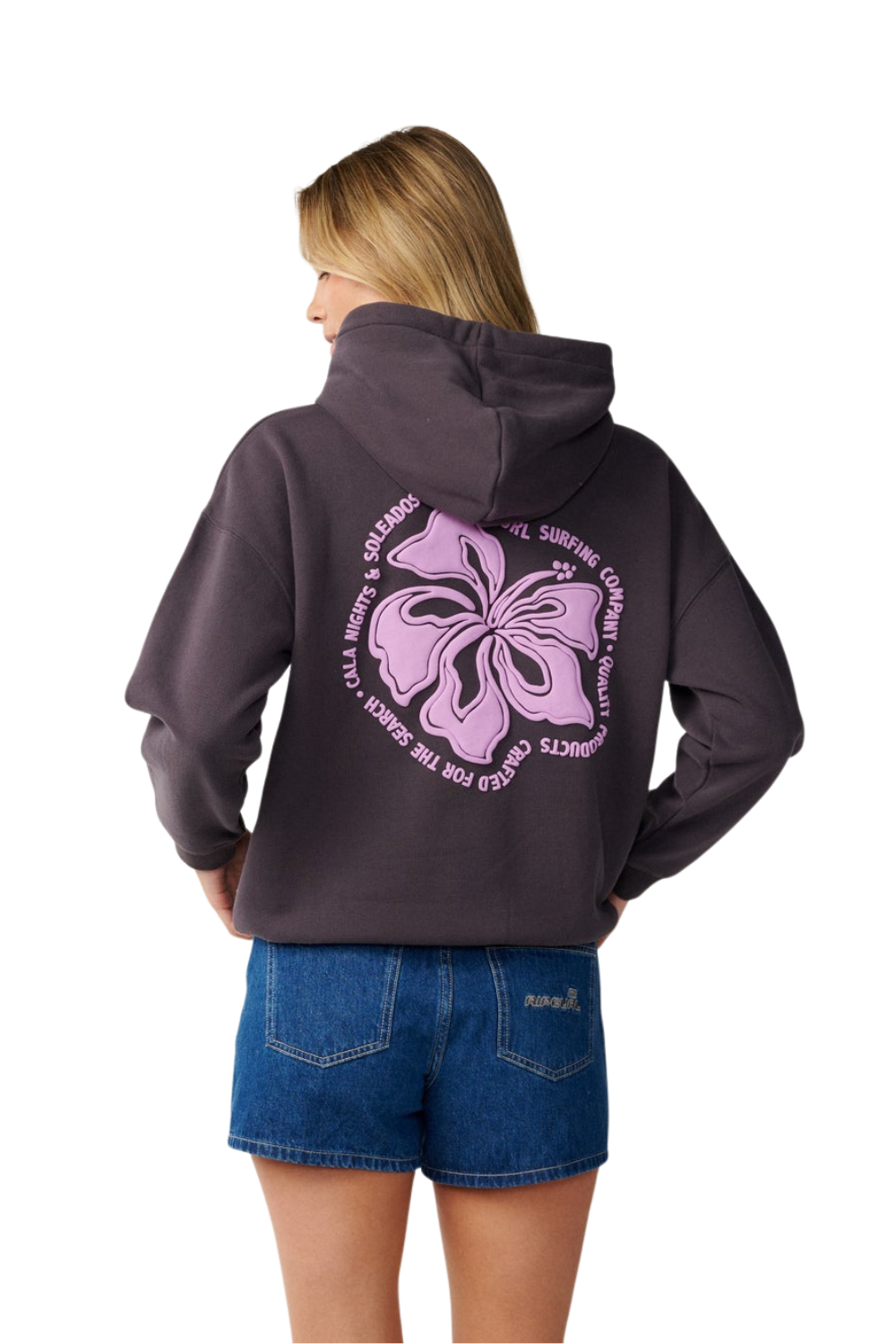 A woman shown from the back wearing a dark charcoal gray hoodie with a large lavender hibiscus flower graphic and text on the back, paired with blue denim shorts, against a plain white background.