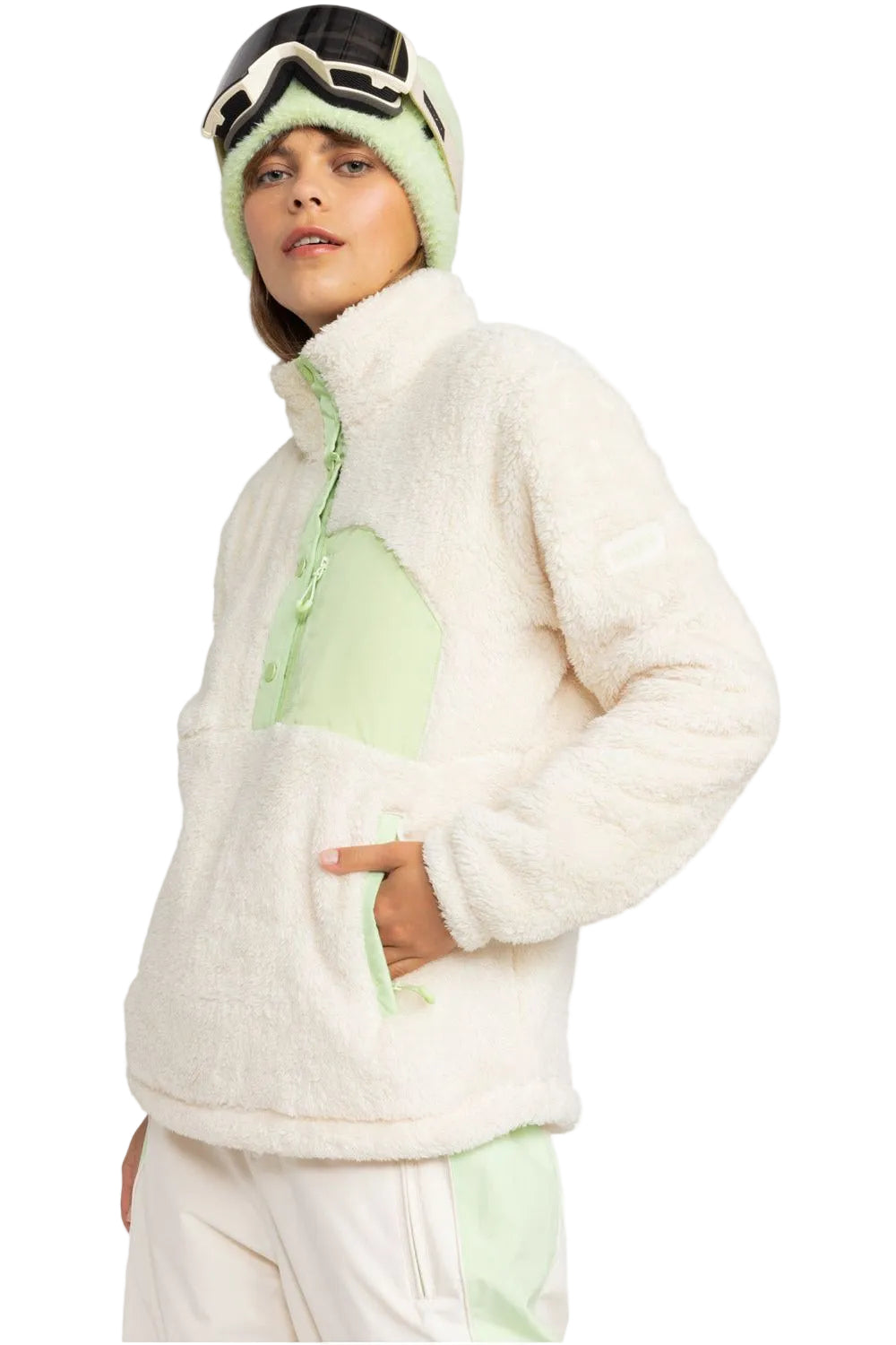 A woman wearing a beige and green fleece jacket with a mock neck, long sleeves, and snap closures. She is also wearing matching beige and green snow pants.