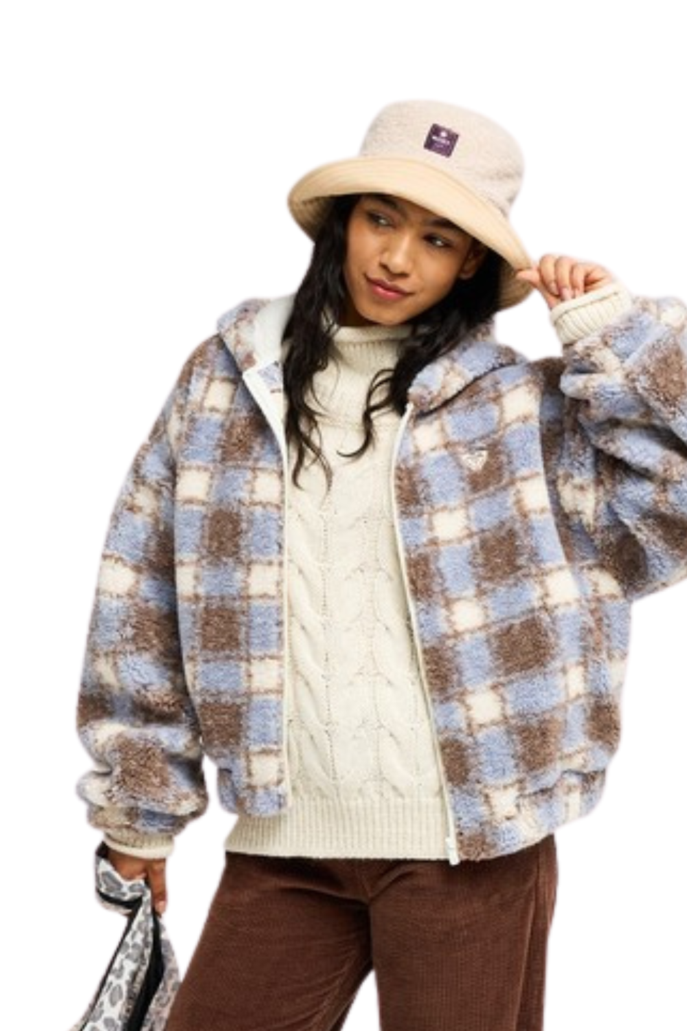 A woman wearing a fuzzy hooded Roxy fleece jacket in light blue, brown, and cream, styled with a cream cable-knit sweater, brown pants, and a beige bucket hat against a white background.