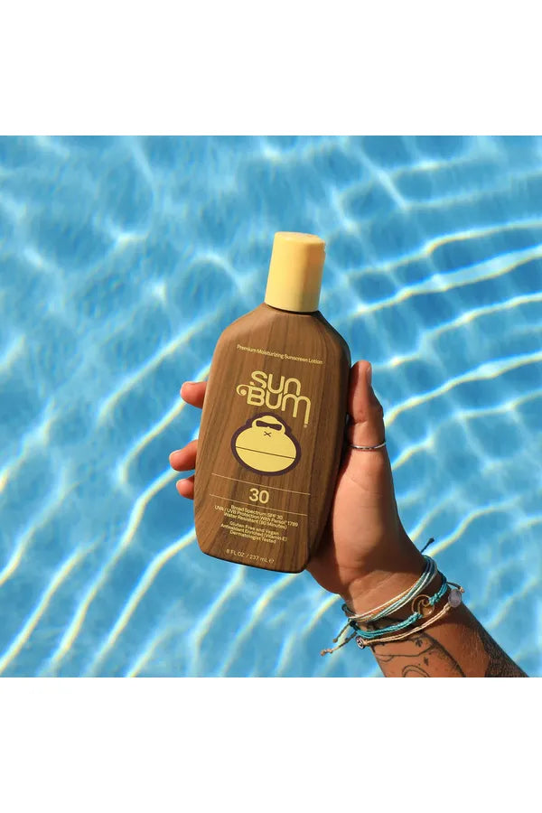 A bottle of Sun Bum Original SPF 30 Sunscreen Lotion held in front of a pool.