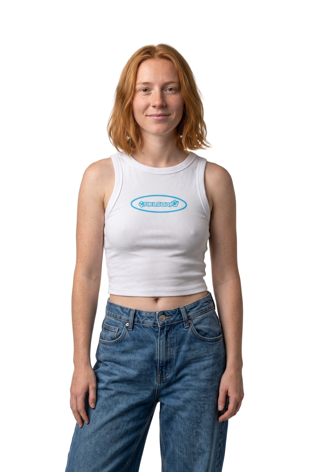 A woman with red hair wearing a white ribbed tank top with a light blue oval 'Tiki Surf' logo on the chest, paired with blue jeans, against a plain white background.