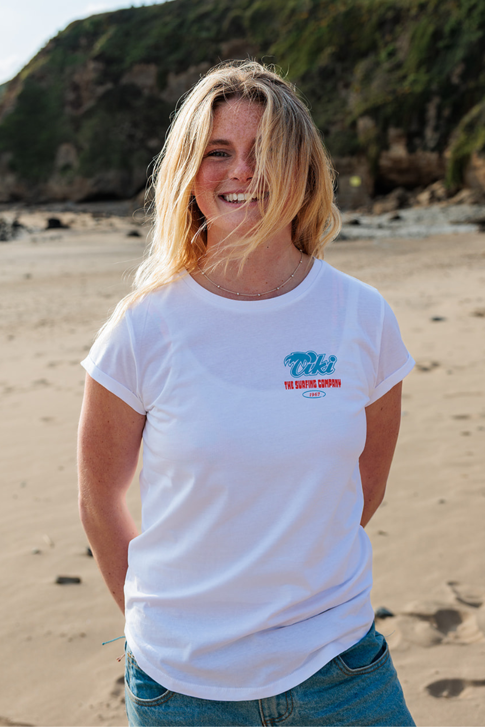 Person wearing a white t-shirt with a Tiki logo on a beach