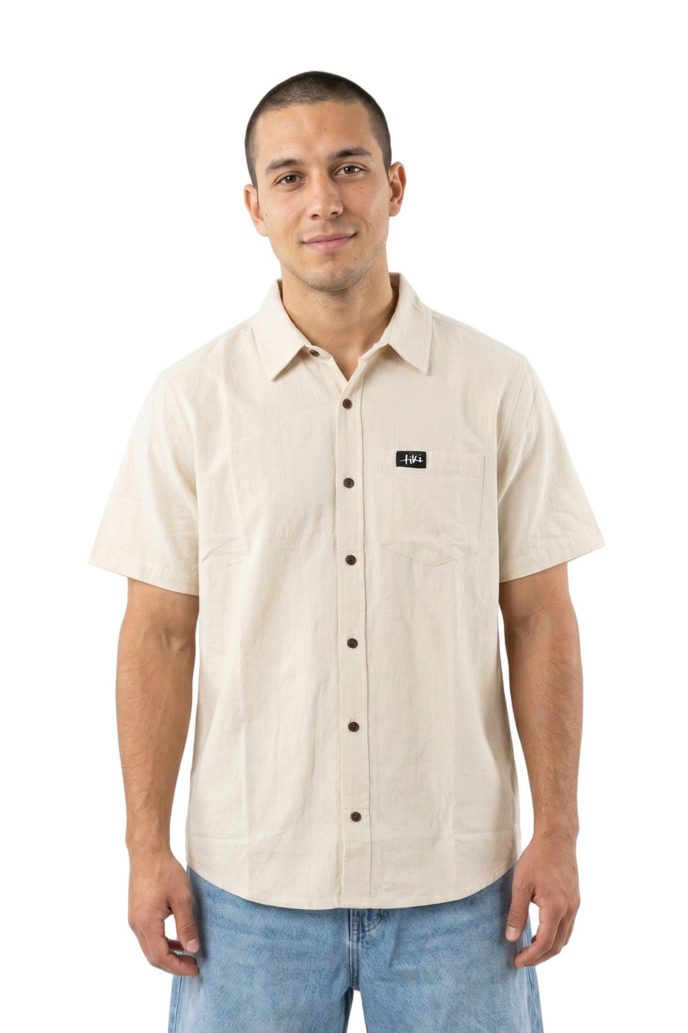 Man wearing a beige short-sleeve button-up shirt with a Tiki logo on a white background