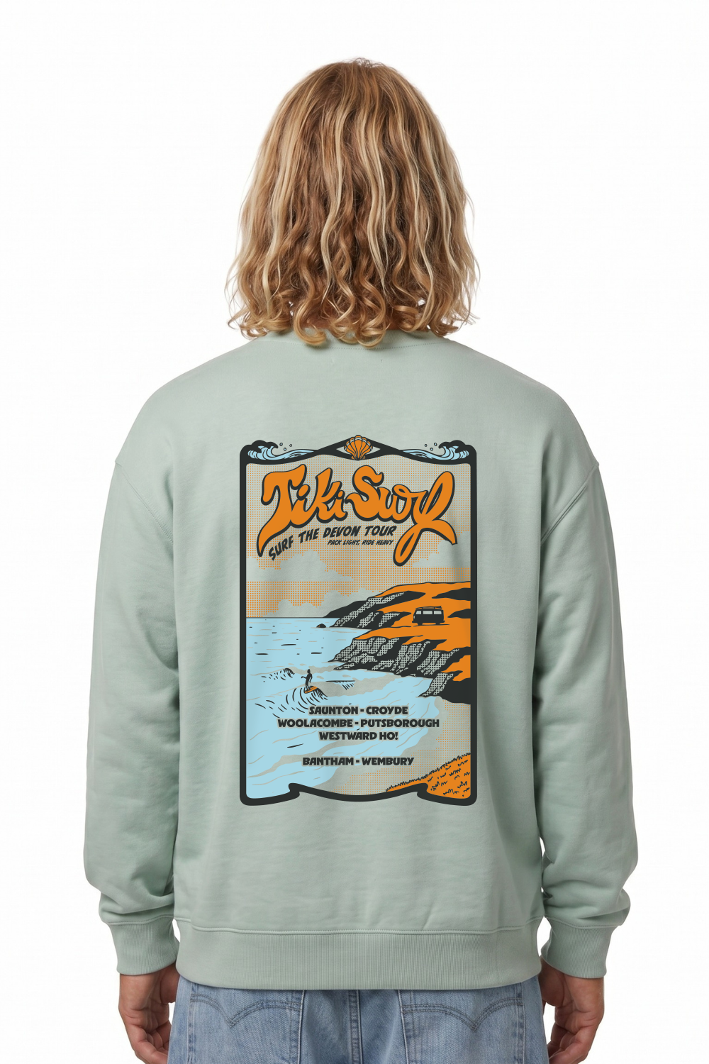 Person wearing a light green sweatshirt in light green. Featuring a bold retro back print showcasing Devon’s famous surf beaches.