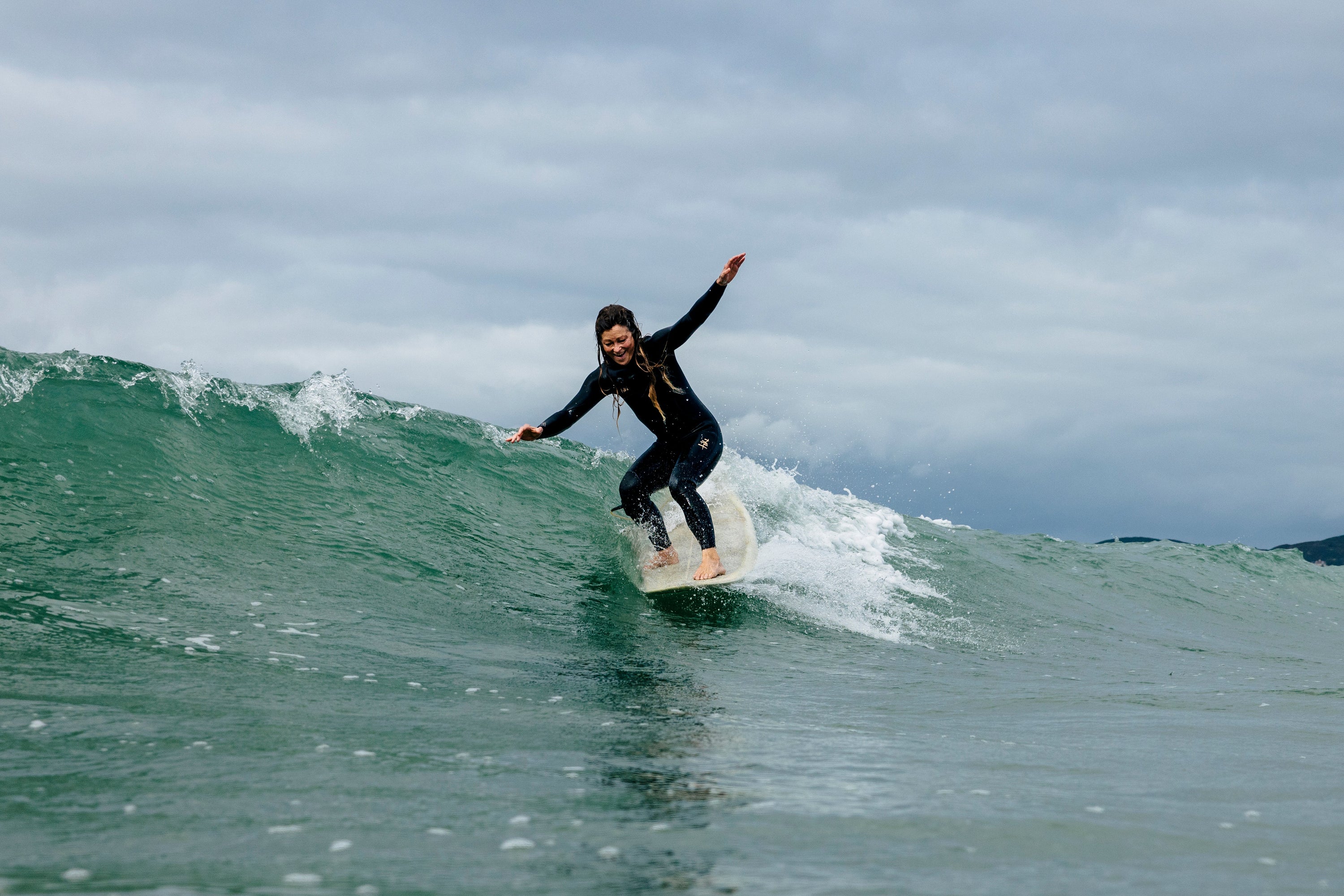 Woman surfing a longboard nose riding in wetsuit on a wave with a cloudy sky