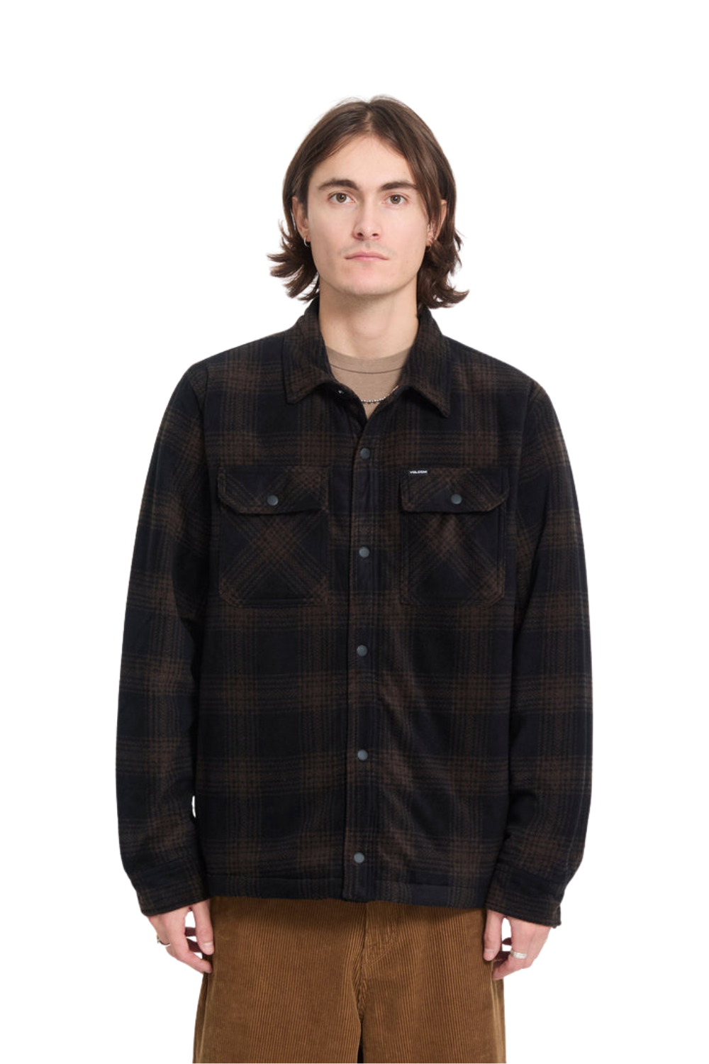 A man wearing a dark brown and black  fleece button-up shirt jacket over a beige t-shirt and brown pants, photographed against a solid white background.