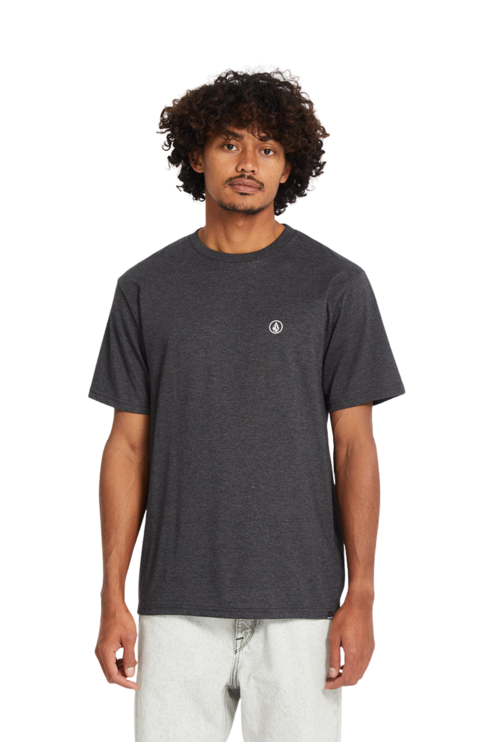 A man wearing a dark heather gray short-sleeve t-shirt with a small white circular Volcom stone logo on the left chest, paired with light gray jeans, against a plain white background.