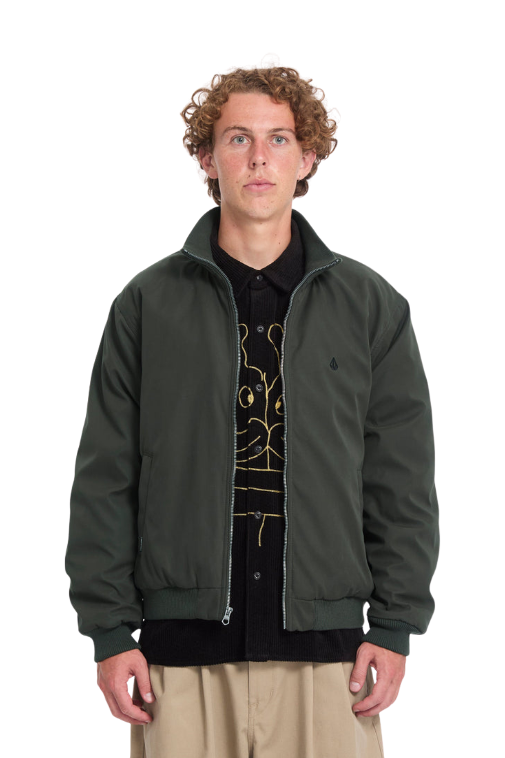 A man wearing an washed black zip-up bomber jacket over a black graphic t-shirt and beige pants, photographed against a solid white background.