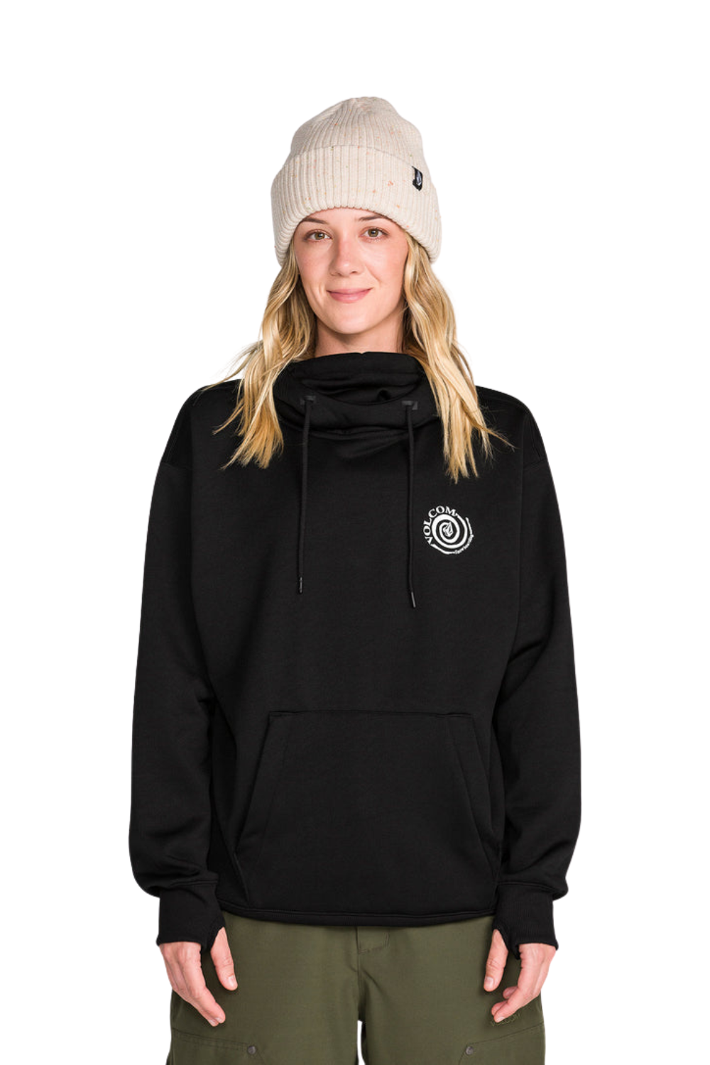 A woman wearing a black cowl-neck pullover hoodie with a white circular logo on the left chest, paired with an off-white beanie and olive green pants, photographed against a solid white background.