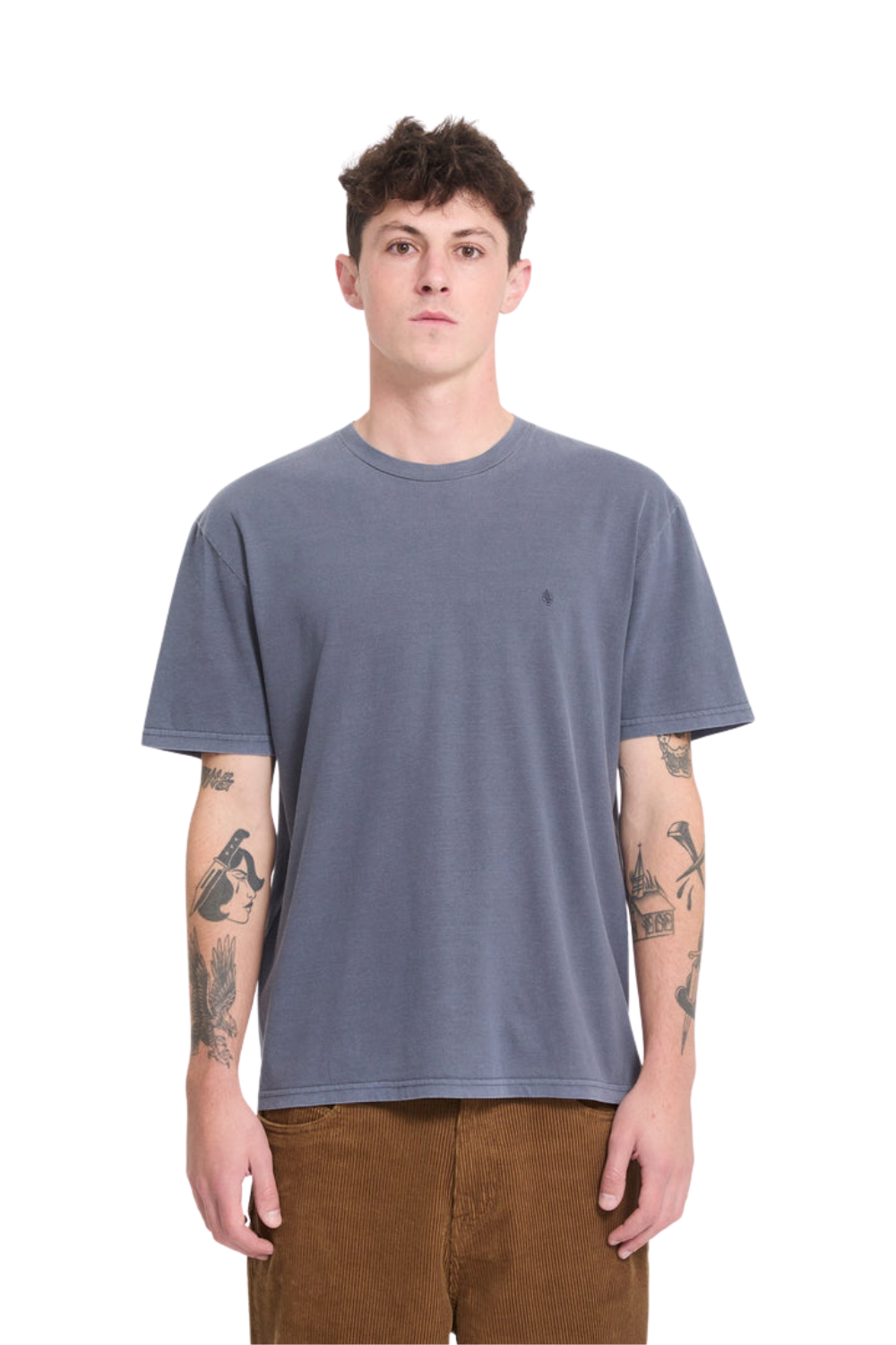 A man wearing a slate blu t-shirt with a small embroidered 'Volcom' stone logo on the chest.