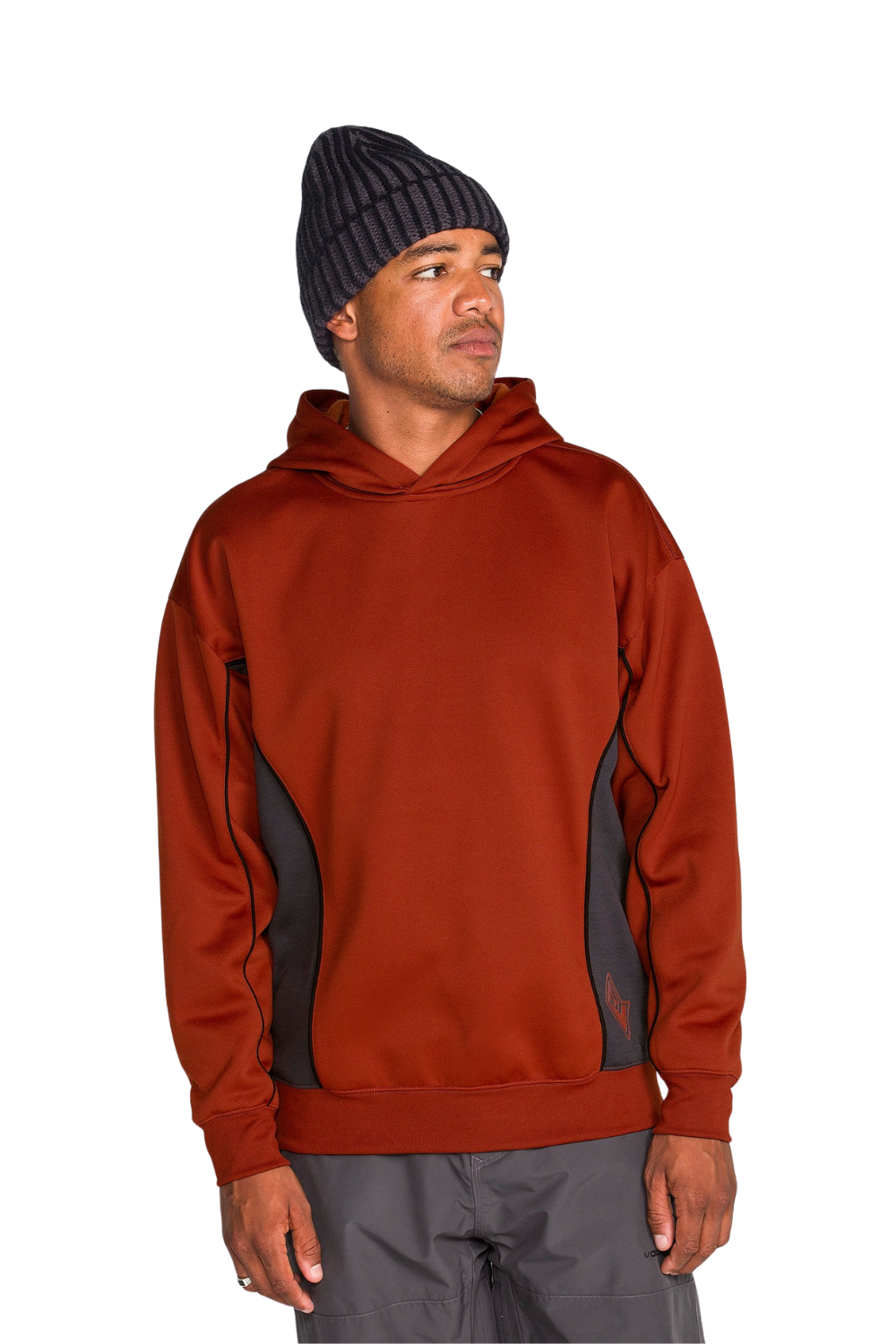 A man wearing a rust-colored pullover Volcom hoodie with dark gray side panels and a dark striped beanie, standing against a plain white background.