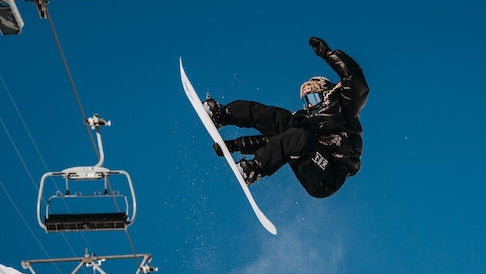 Person snowboarding off a ramp with a ski lift and blue sky in the background